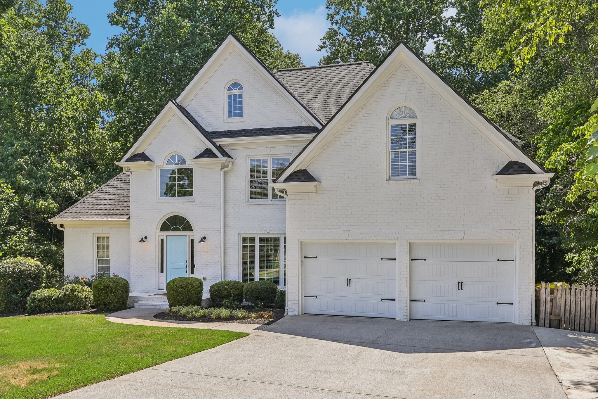 White brick two-story house with a blue front door, arched windows, double garage, and landscaped front yard.