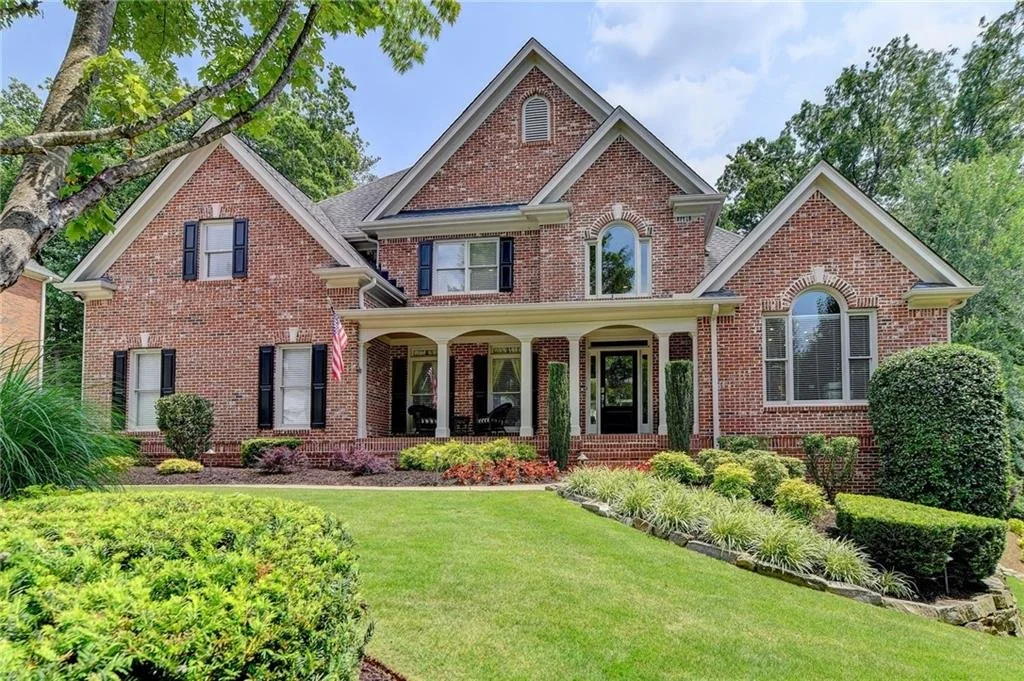 Two-story red brick house with gabled roof, arched windows, and landscaped front yard.