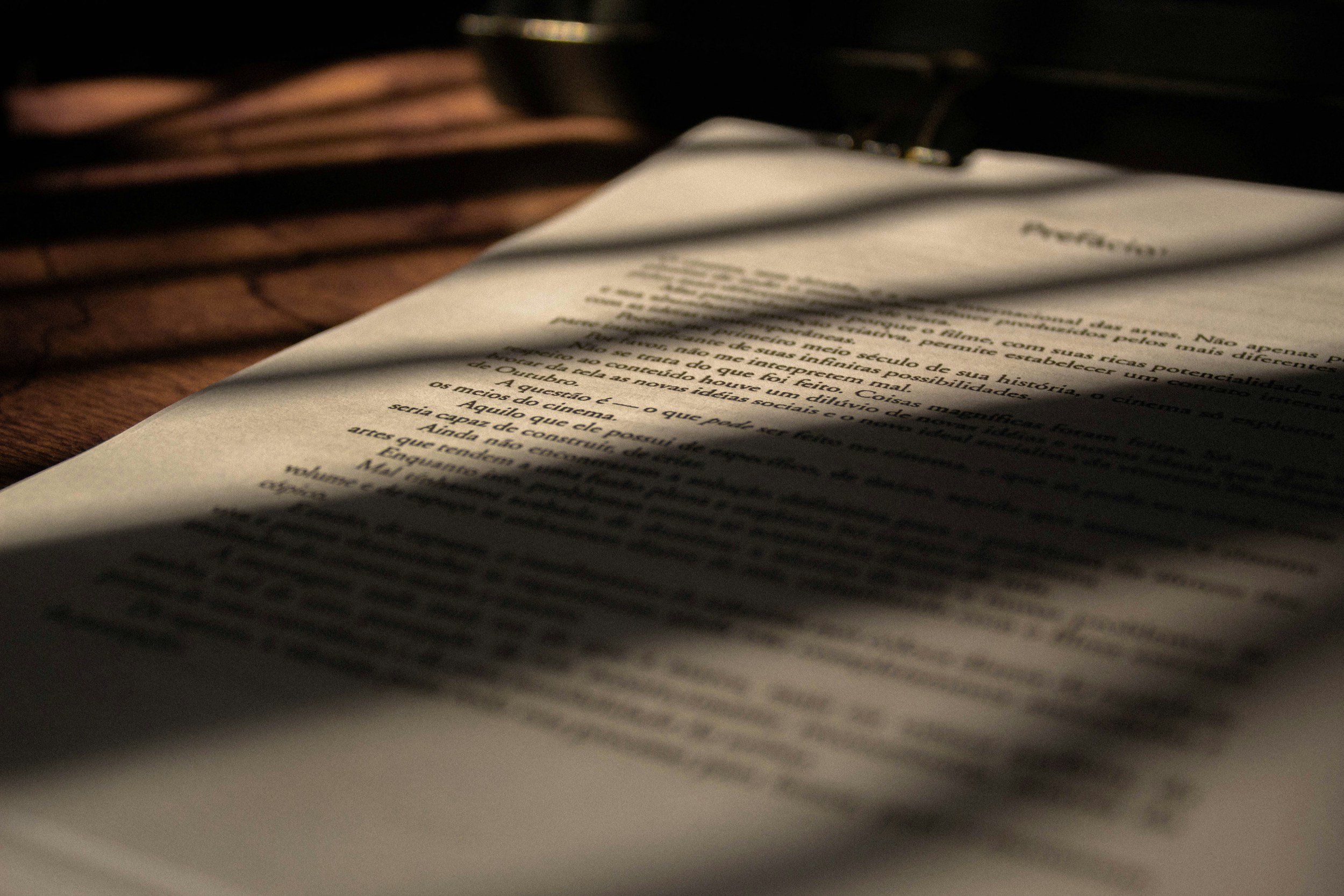 A close-up of a printed script or manuscript on white paper, placed on a wooden surface, with shadows cast across it from a nearby window.