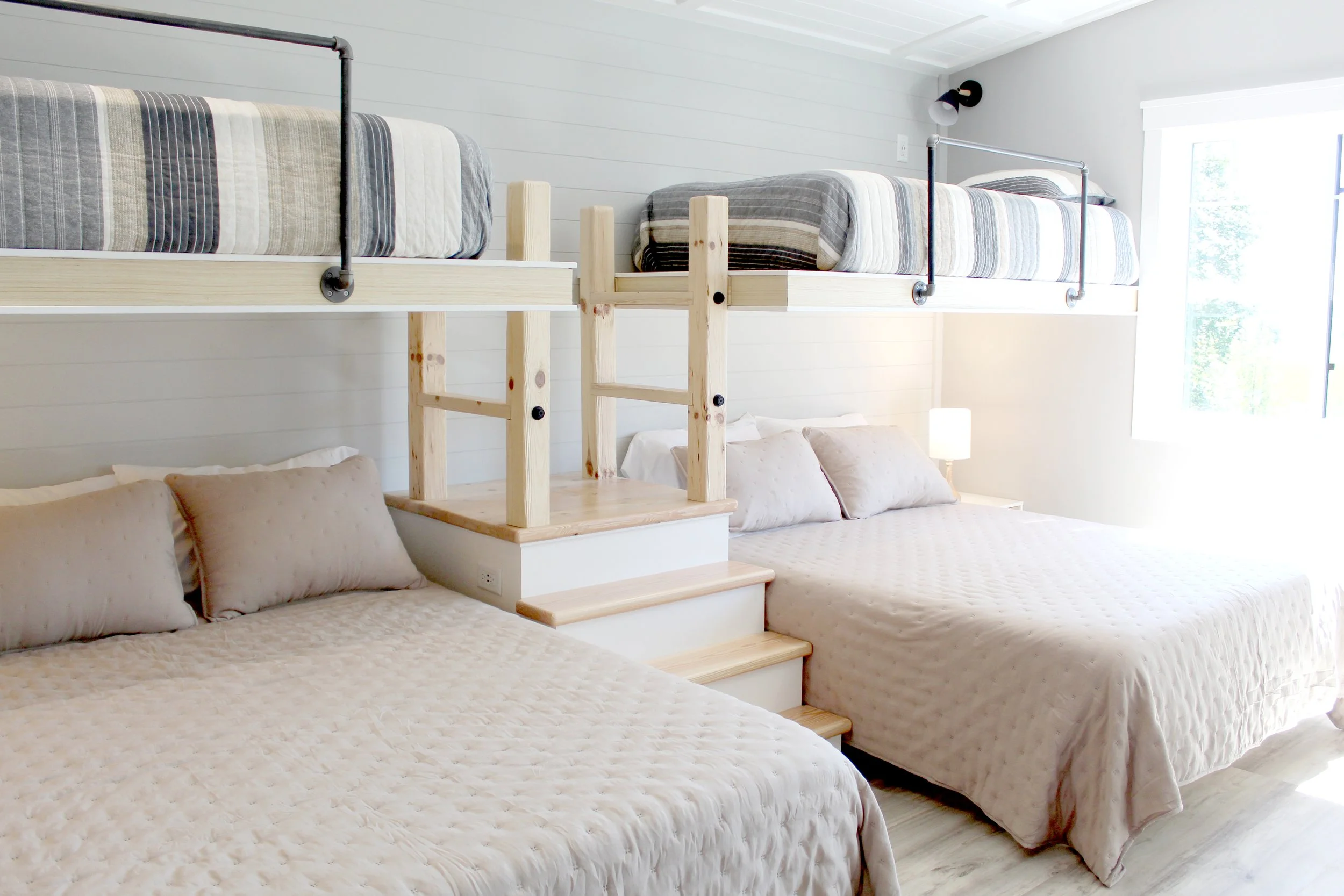 Cozy bedroom with two beds, one traditional and one elevated with a wooden ladder, white walls, and a large window letting in natural light.