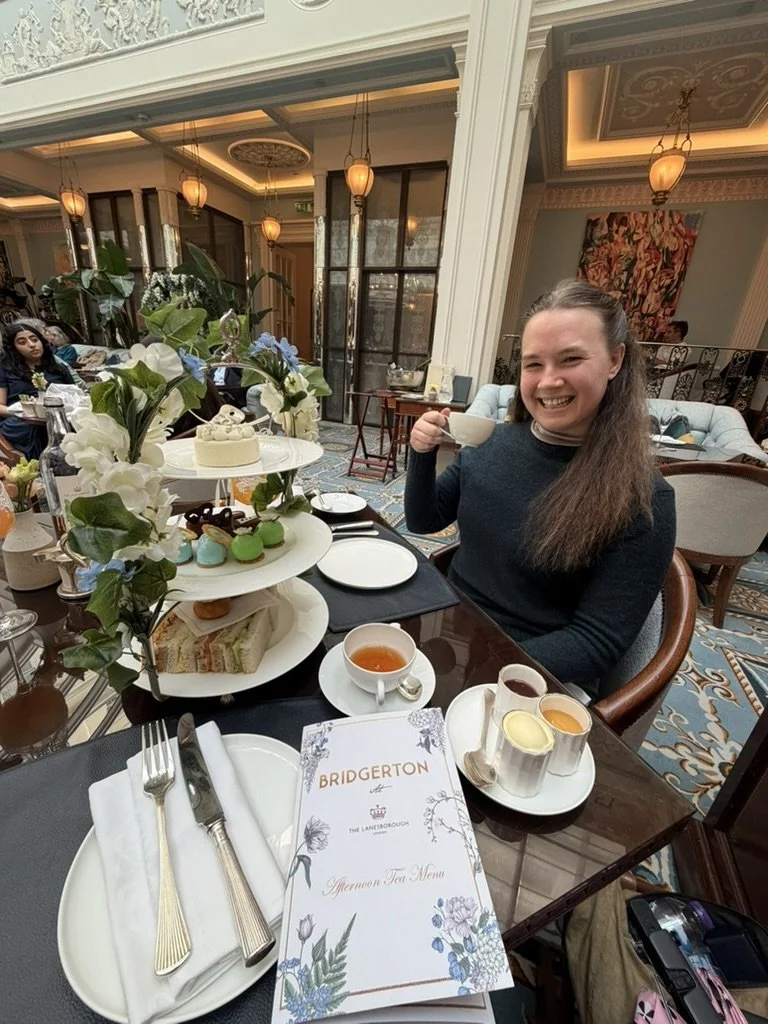 A woman in a green sweater is holding a teacup in front of an afternoon tea in London.
