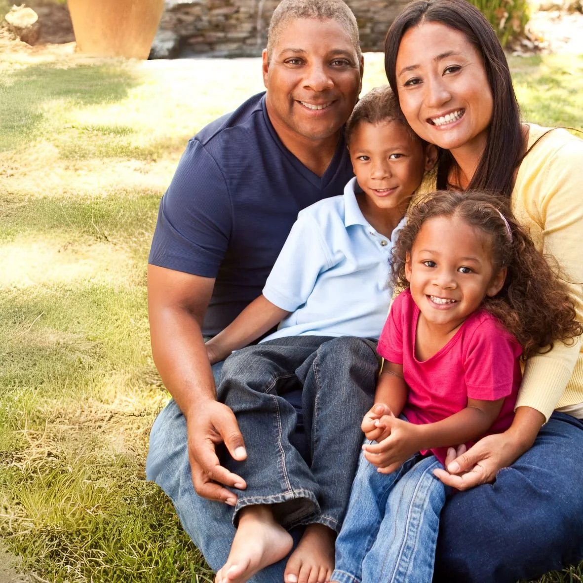 Photo of a family of four people: two adults and two children outside in the grass.