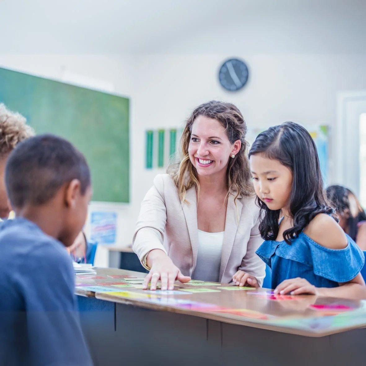 Photo of a smiling teacher sitting with two young students at a desk.
