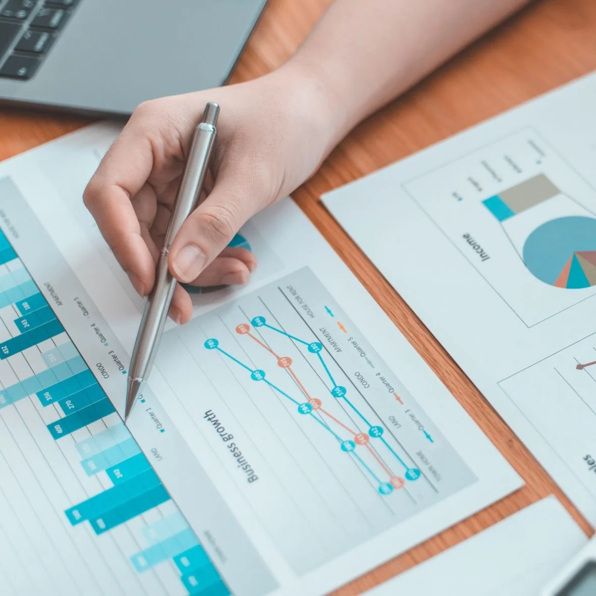 Photo of a hand holding a pencil over a paper printed with graphs and charts.
