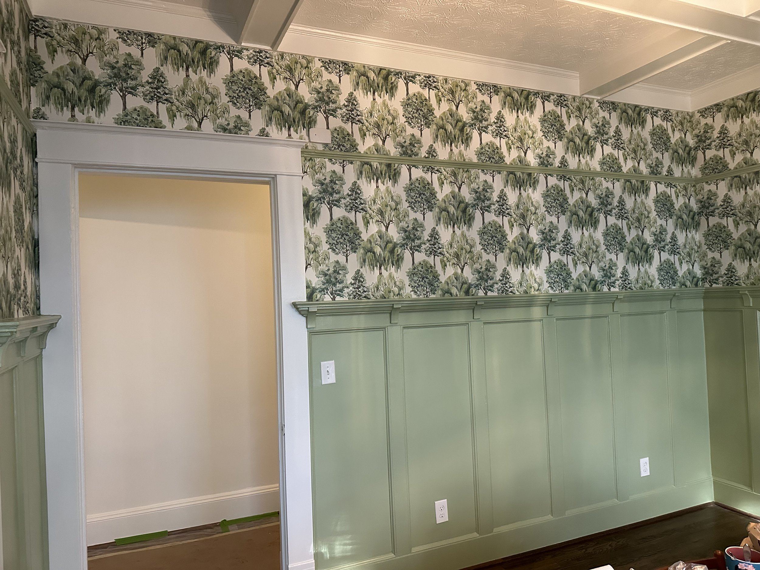 Room with green wainscoting and wallpaper featuring trees, with door opening to an empty space.