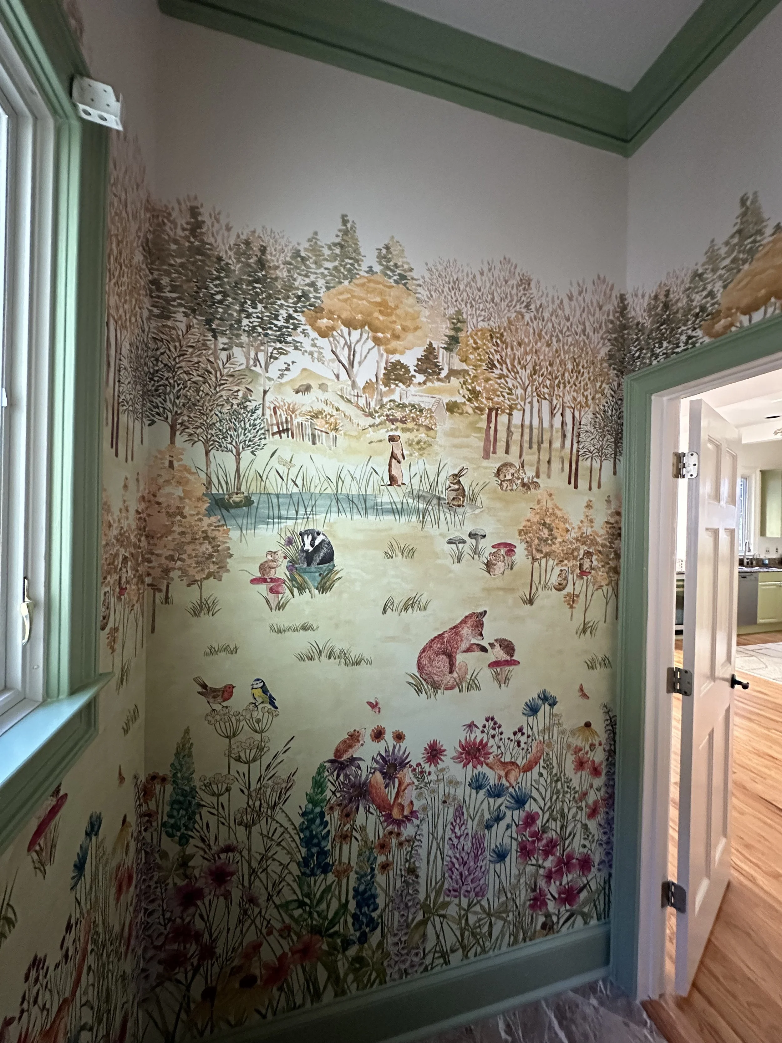 Colorful mural of a nature scene featuring trees, a pond with animals like raccoons, otters, birds, and a bear, with flowers and grass in the foreground.