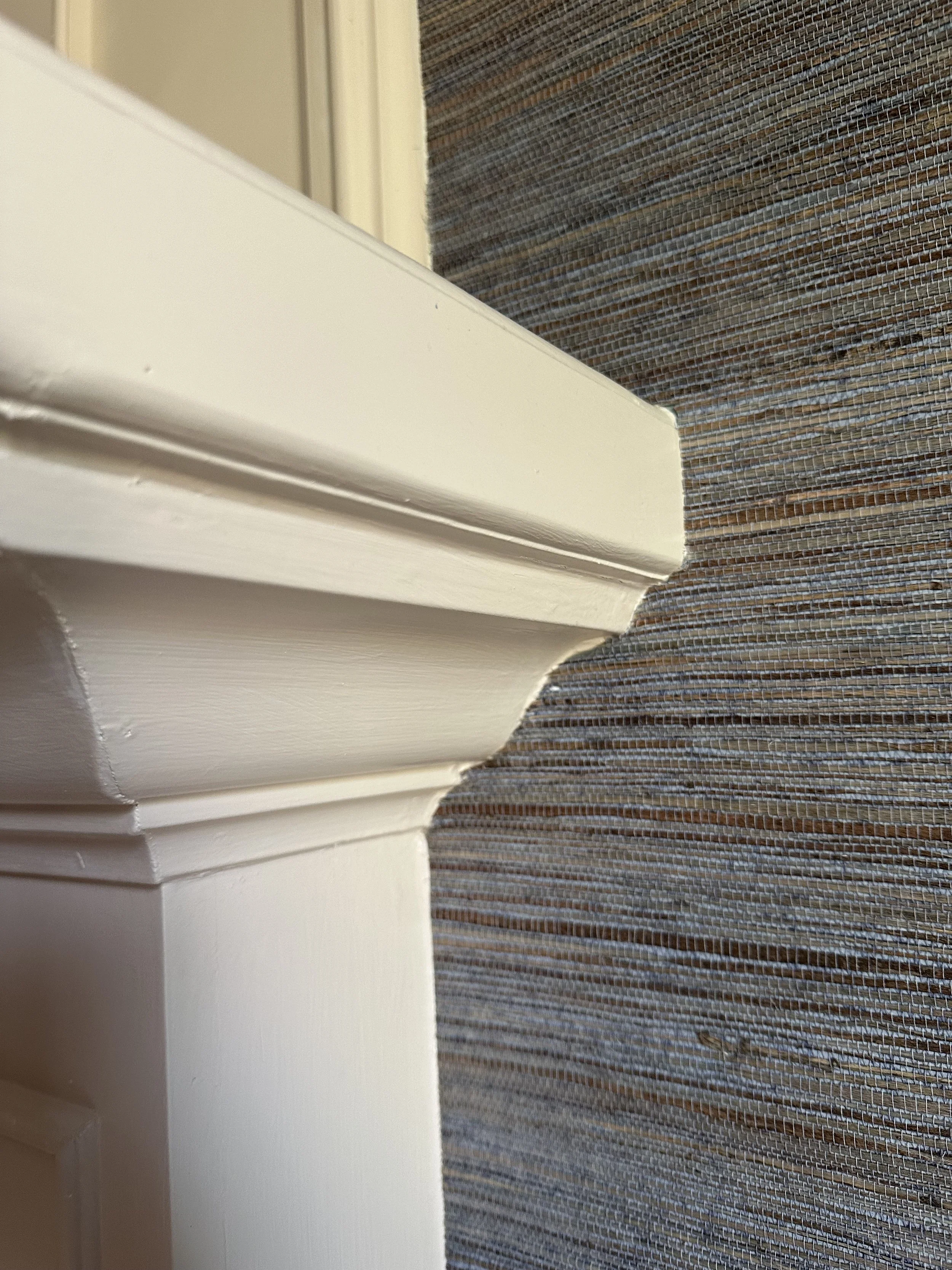 Close-up of the corner of a white wooden window frame next to textured fabric or window screen.