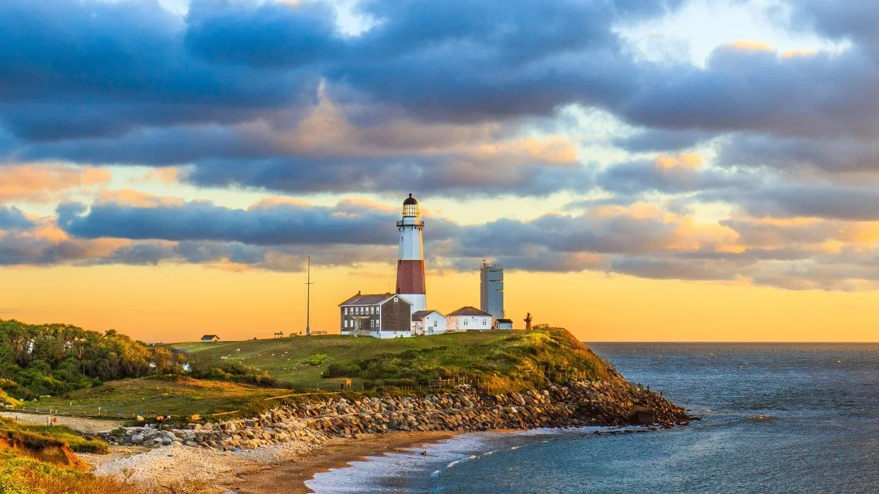 Lighthouse on a cliff overlooking the ocean during sunset with cloudy sky.