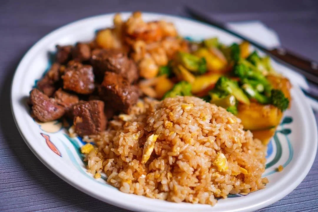 A plate of Chinese fried rice with scrambled eggs, dark soy sauce, alongside beef chunks, stir-fried vegetables, and broccoli.