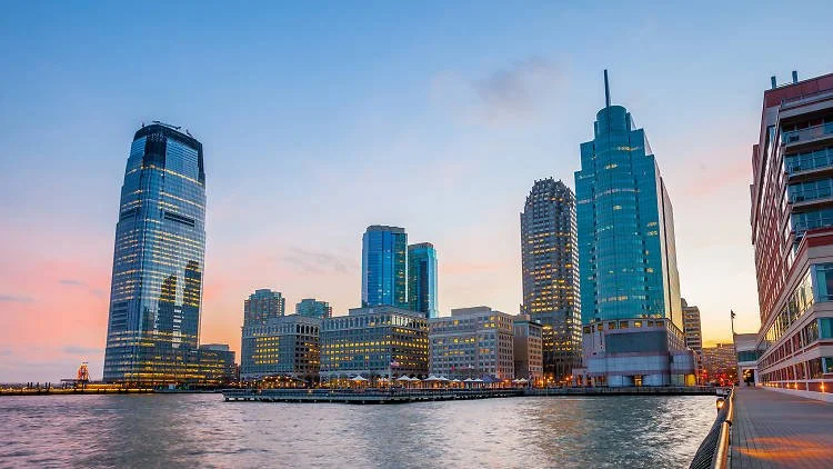 City skyline with tall modern buildings near a waterway during sunset.