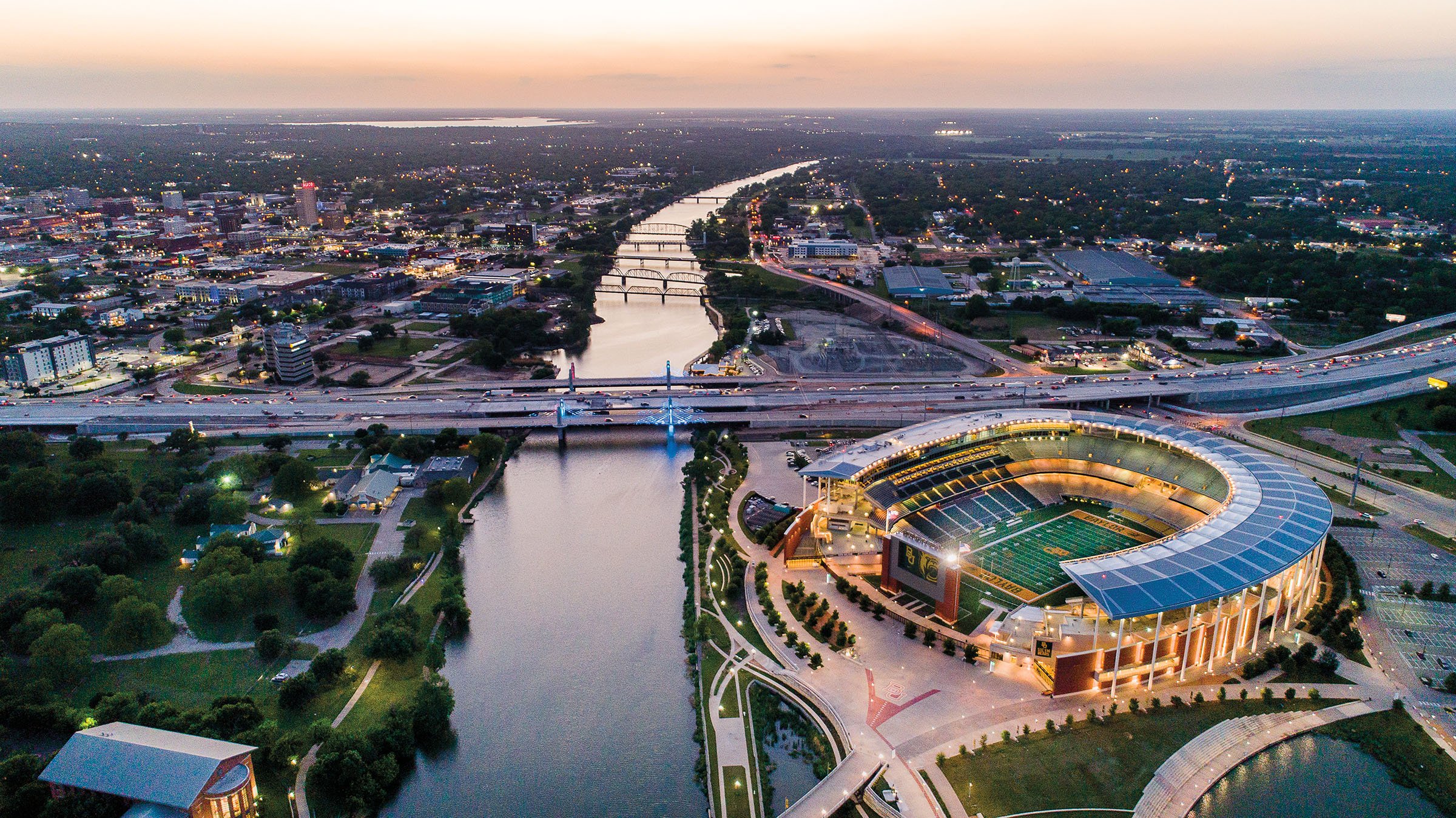 Aerial view of a city at dusk with a large football stadium and a river running through the city.