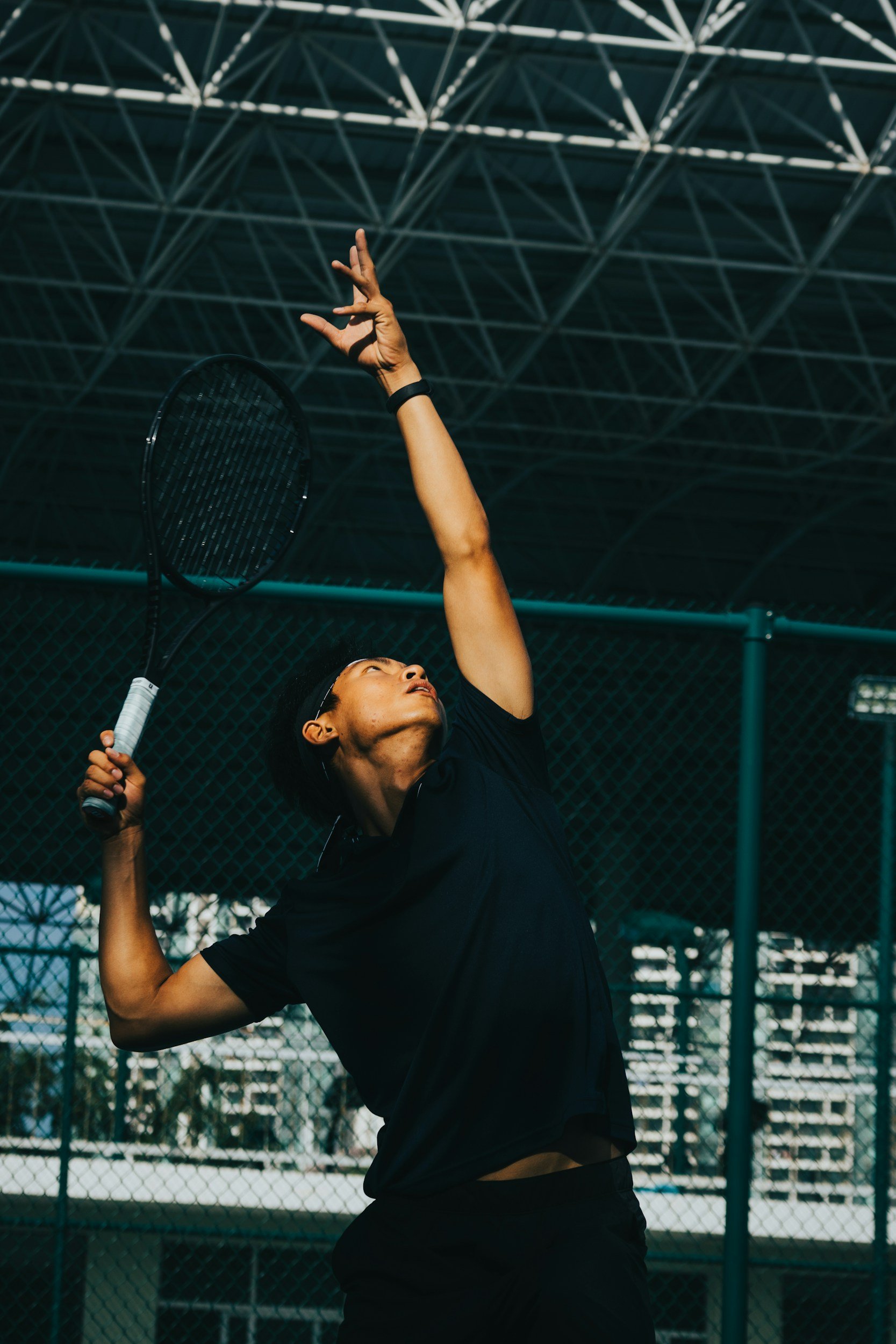 Tennis player preparing to serve on an outdoor court under a canopy.