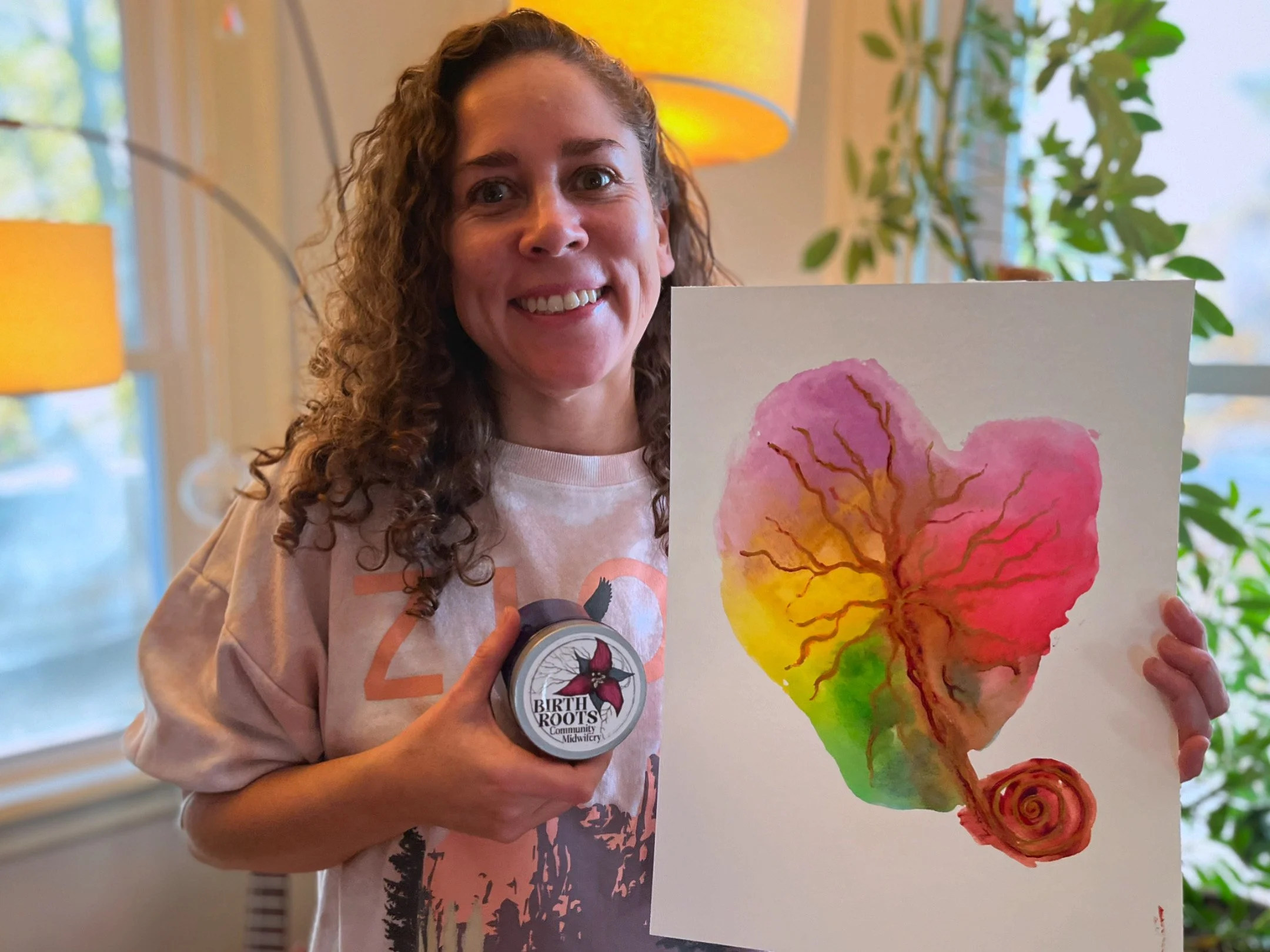 Coté smiling wide, holding up a jar with Birth Roots logo and a placenta print