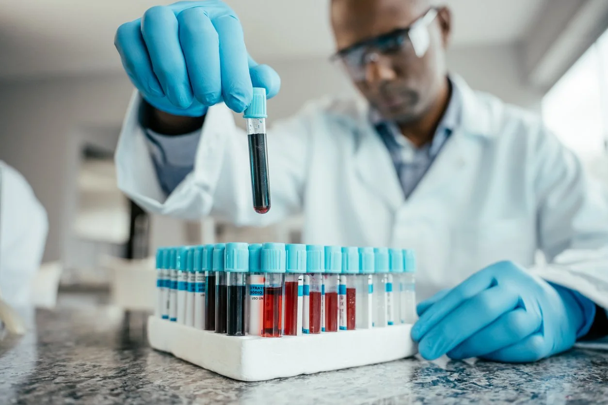 A scientist in a laboratory using a pipette to transfer a blood sample into test tubes arranged in a rack.