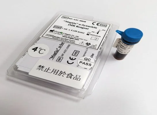 A transparent plastic container with a medical test label inside and a small vial with a blue cap beside it on a white background.
