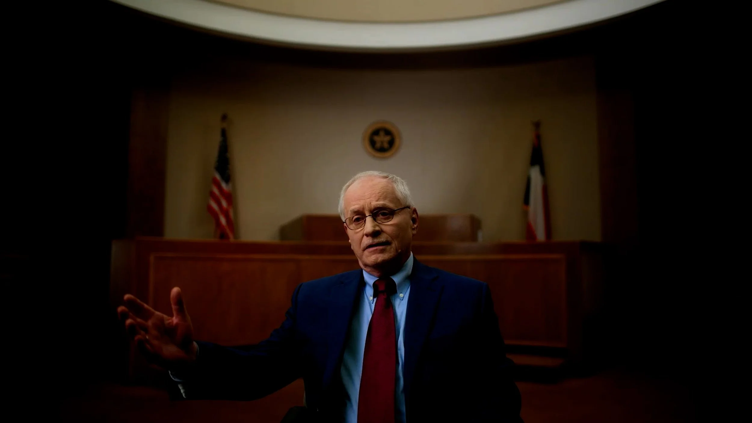 Man in a courtroom setting with flags