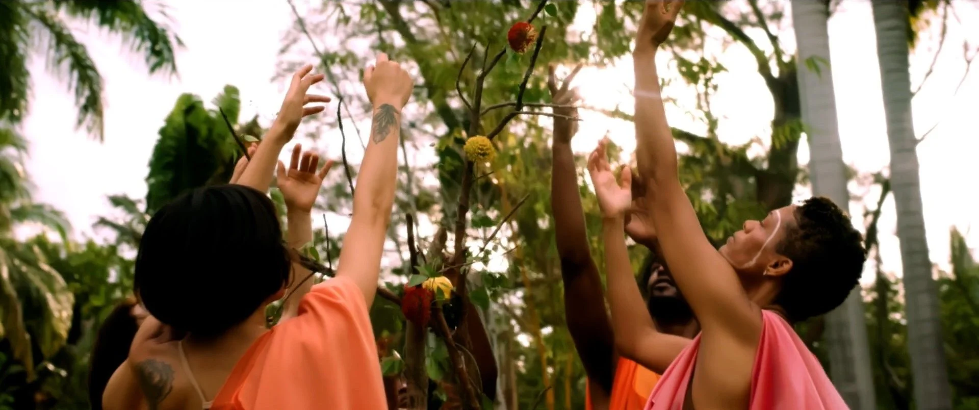 Group of people reaching for branches with colorful flowers in a lush, outdoor setting.