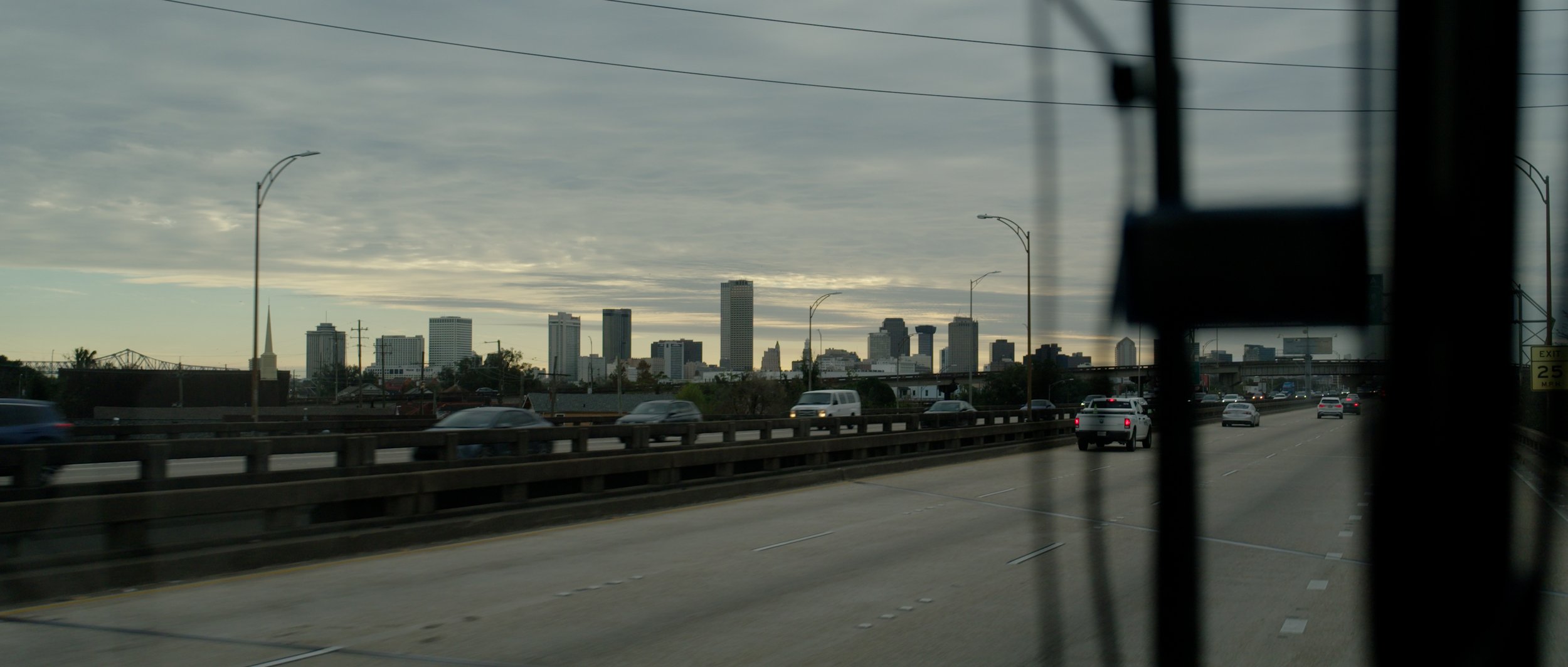 City skyline viewed from a highway with cars, under cloudy skies.
