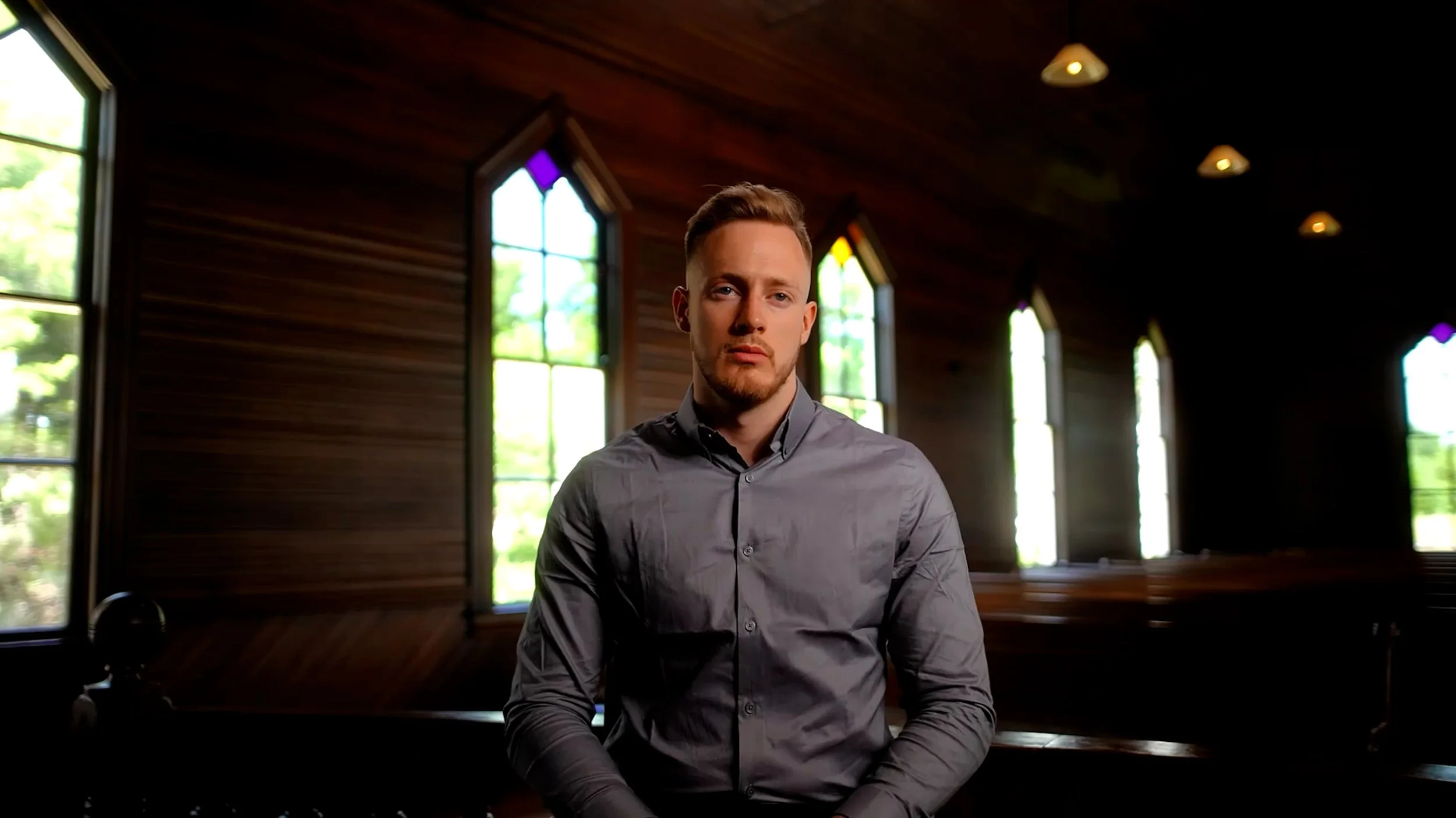 Man sitting in a dimly lit church with stained glass windows.