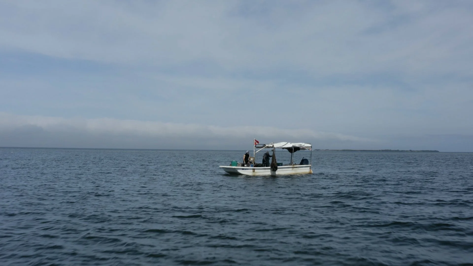 Small boat with a canopy on a calm ocean under a cloudy sky.