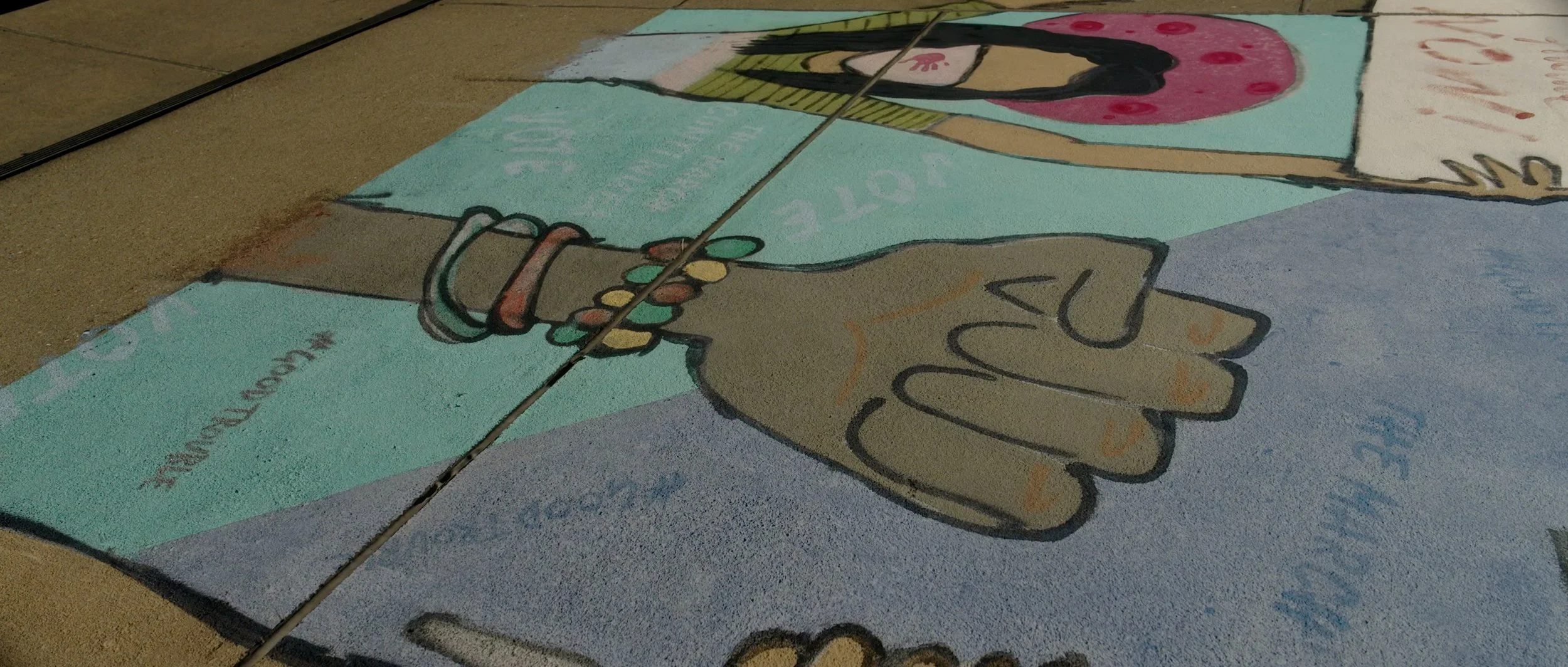 Colorful chalk drawing of two hands shaking, with various words and symbols around them, on the ground.