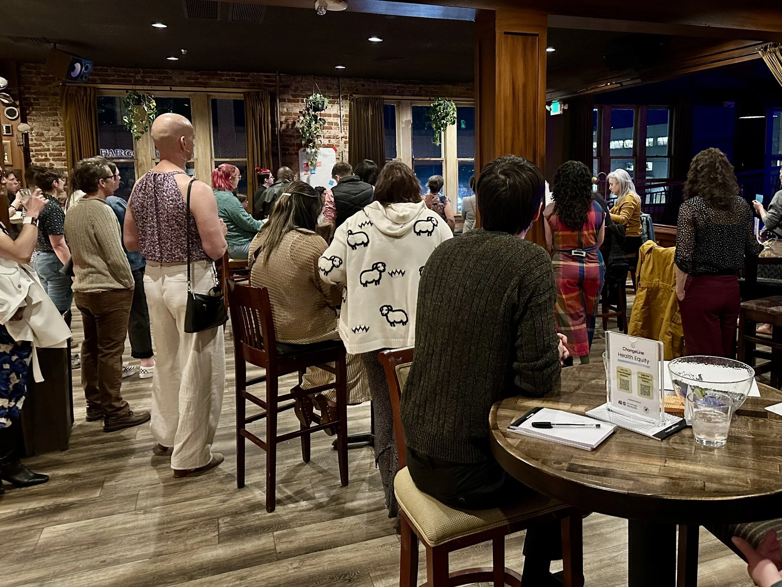  A welcoming room full of healthcare providers sitting at or standing around tables and mingling with each other. 