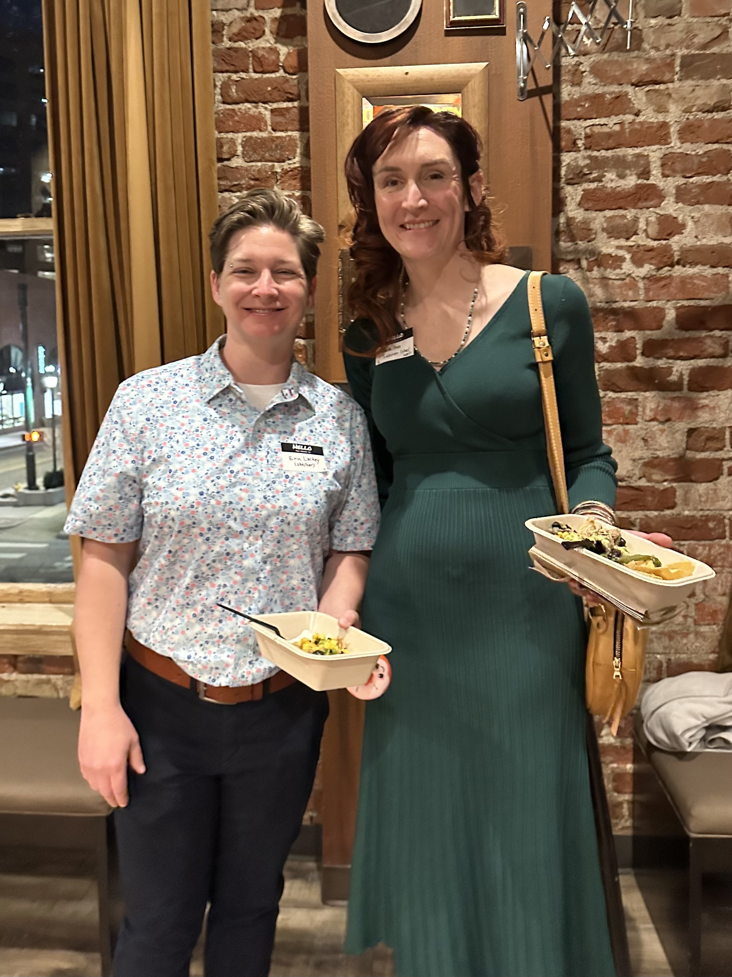  Two people standing before a brick wall smile warmly for the camera. 