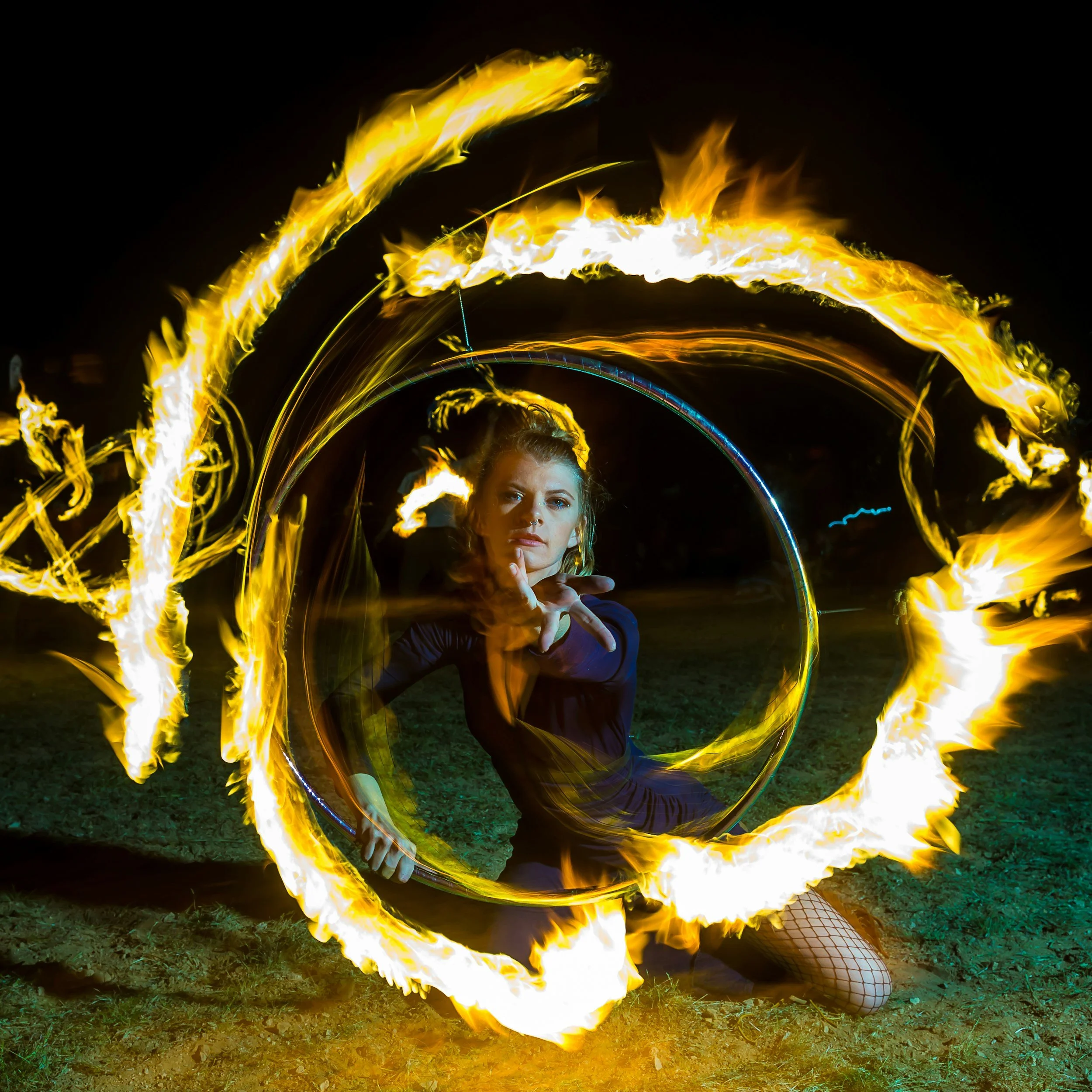 Fire performer creating a striking visual display surrounded by a circle of flames with a hula hoop at an evening event.