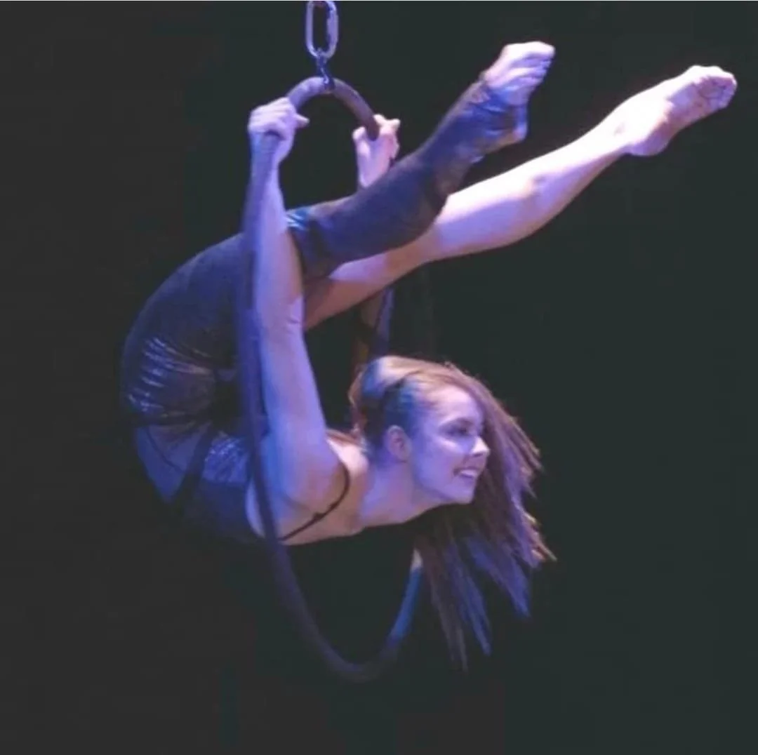 Contortionist performing an elegant backbend in an aerial hoop during a dramatic circus aerial performance.