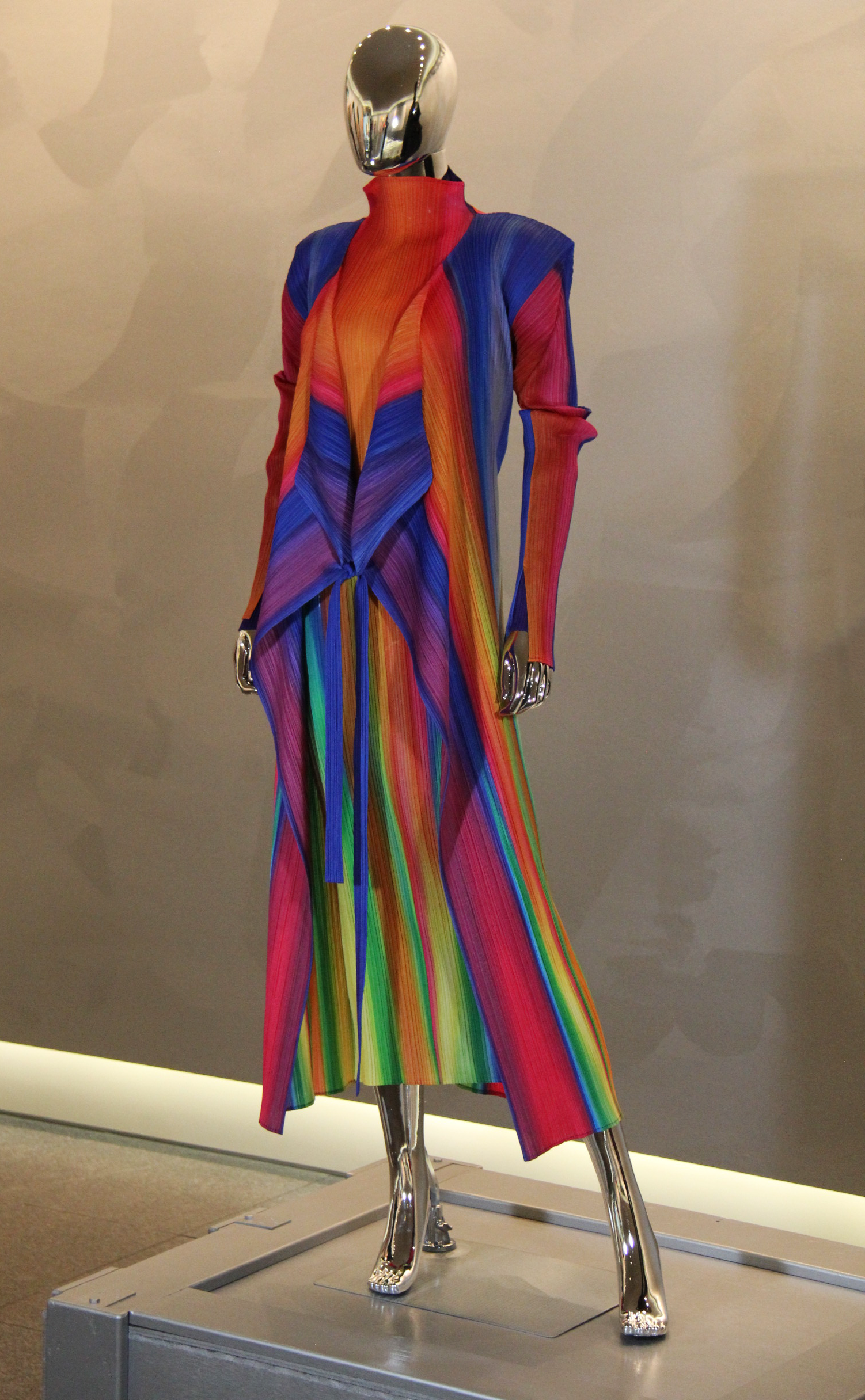 A metallic mannequin displaying a colorful, long-sleeved, high-neck dress with rainbow vertical stripes.