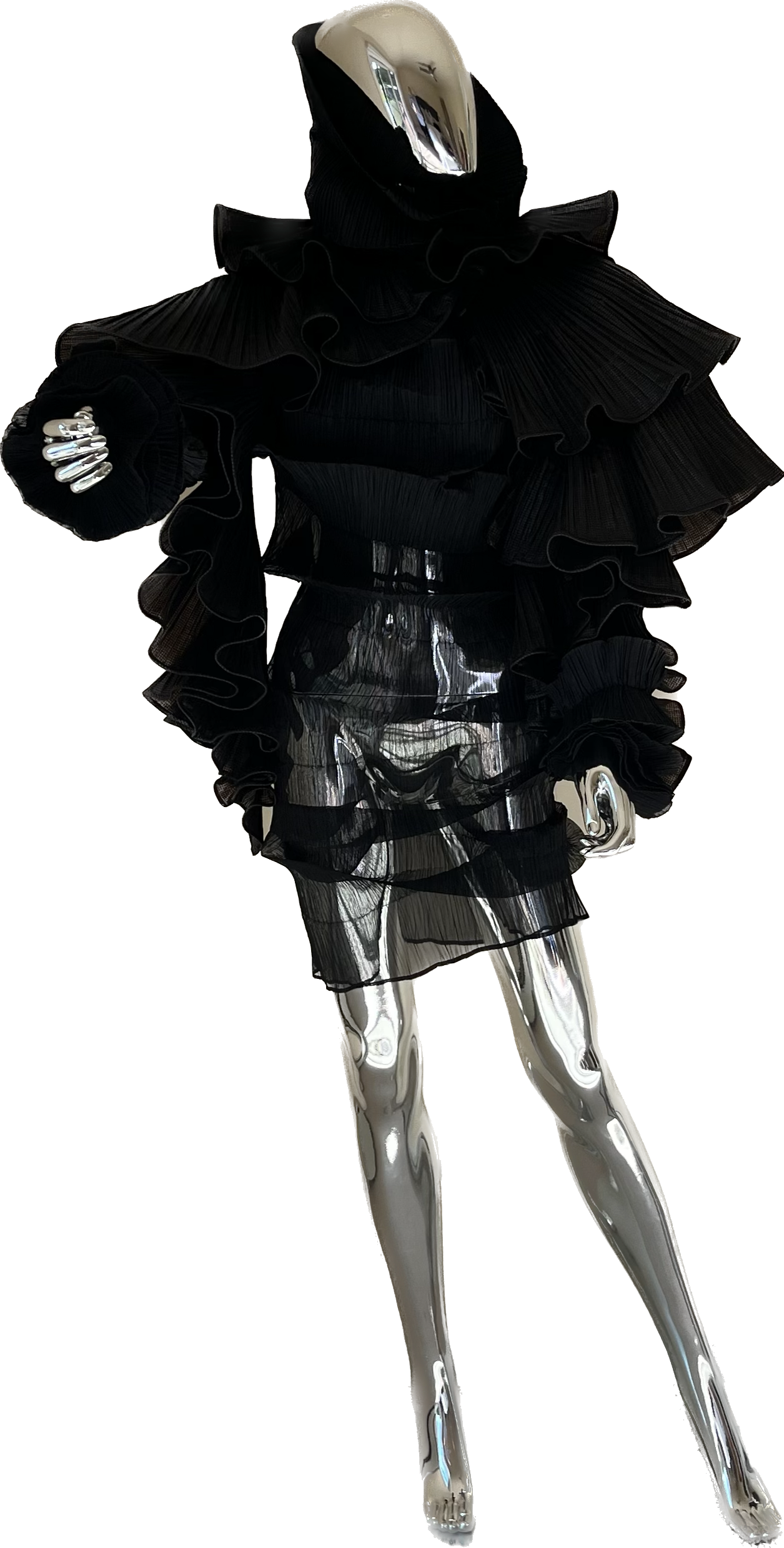 A reflective, chrome mannequin dressed in a high-fashion black outfit with ruffled layers, including a ruffled collar and sheer skirt, standing with hands near hips.