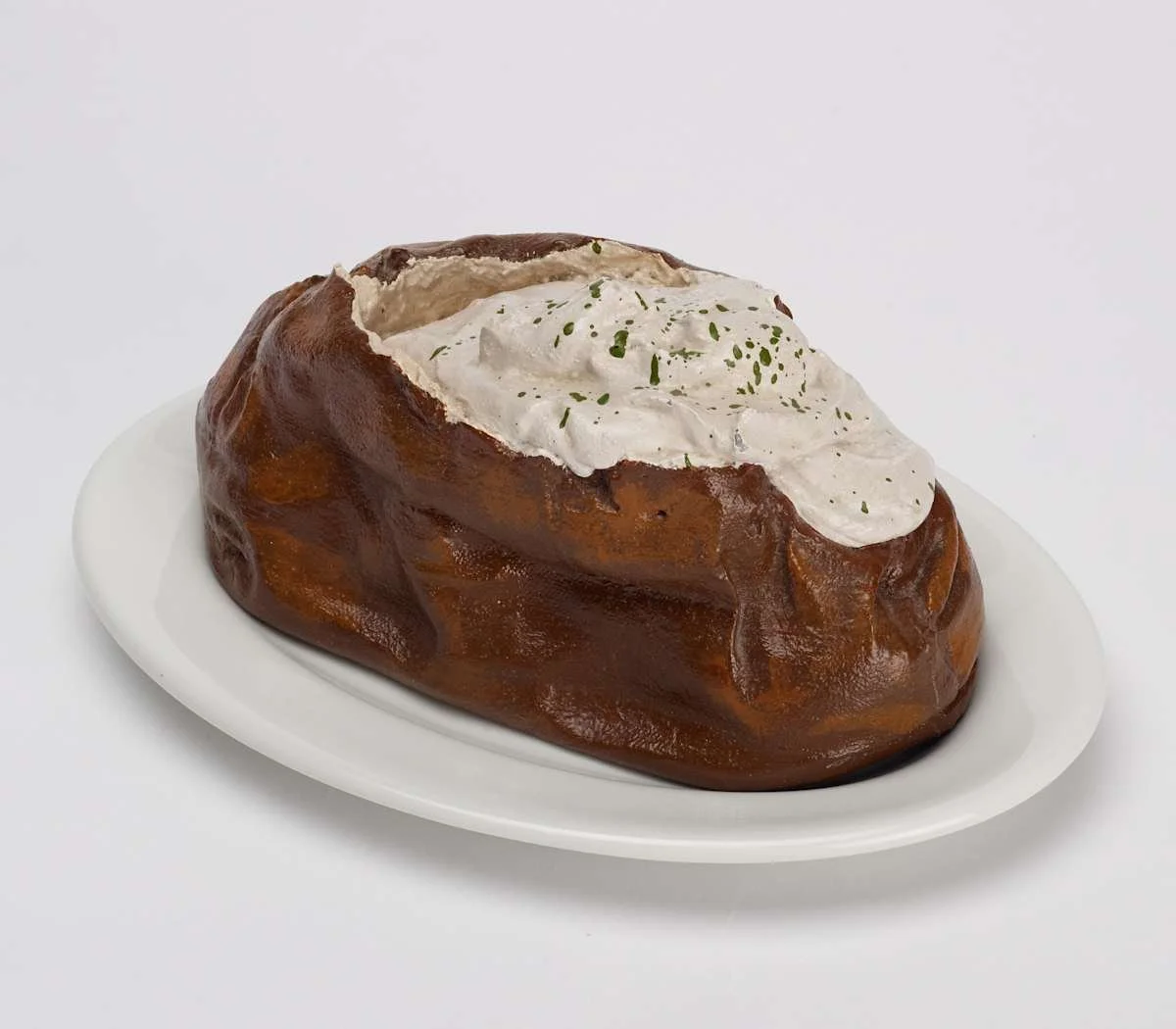 Baked potato topped with sour cream and garnished with herbs on a white plate.