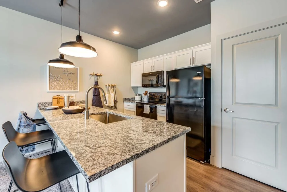 Modern kitchen with granite counter island, black refrigerator, microwave, and white cabinetry, with seating and pendant lighting.