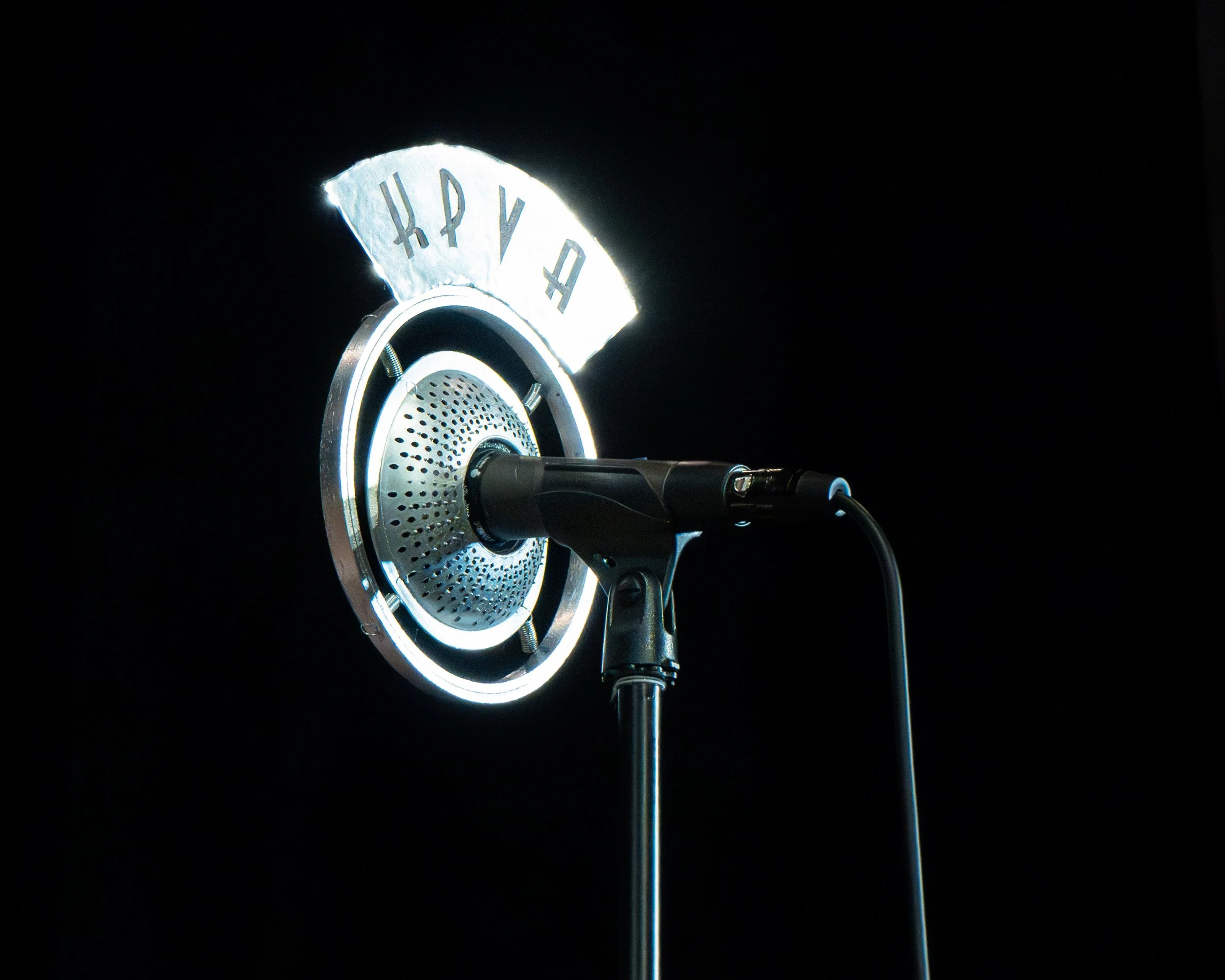 An anniversary number-shaped cake topper illuminated on a microphone stand against a black background.