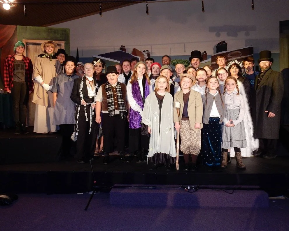 Group of children and adults in theatrical costumes on stage for a play or performance.