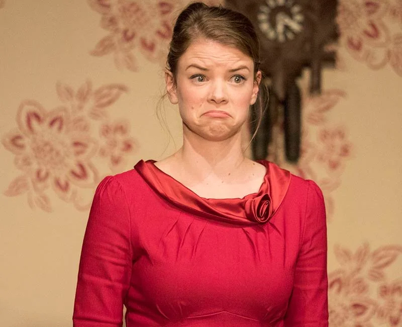 Woman with brown hair in a red dress making a sad or disappointed facial expression indoors.