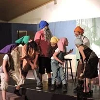Children performing on stage with colorful umbrellas and hats.