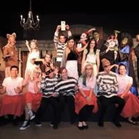 Group of people dressed in costumes on stage, some taking photos, in a theatrical setting.