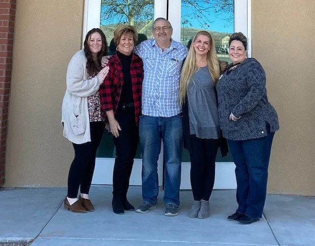 Five people standing together outside in front of a glass door, smiling for a photo.