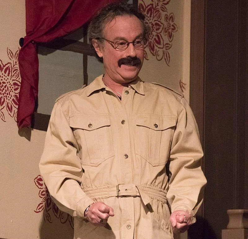 Man dressed as Steve Carell's character Michael Scott from The Office, wearing a beige jumpsuit, standing indoors with a surprised or excited expression.