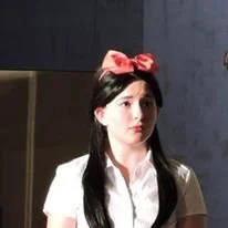 A young woman with long dark hair wearing a white shirt and a pink headband with a bow.