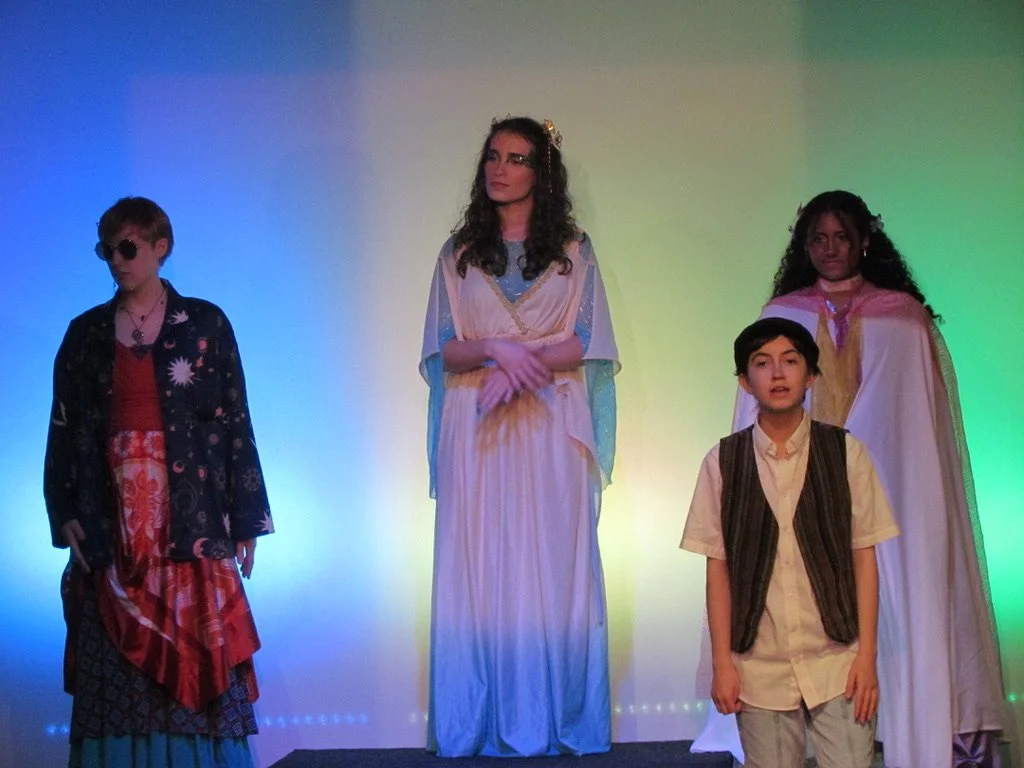 Group of children in costumes on stage with colored lighting background.