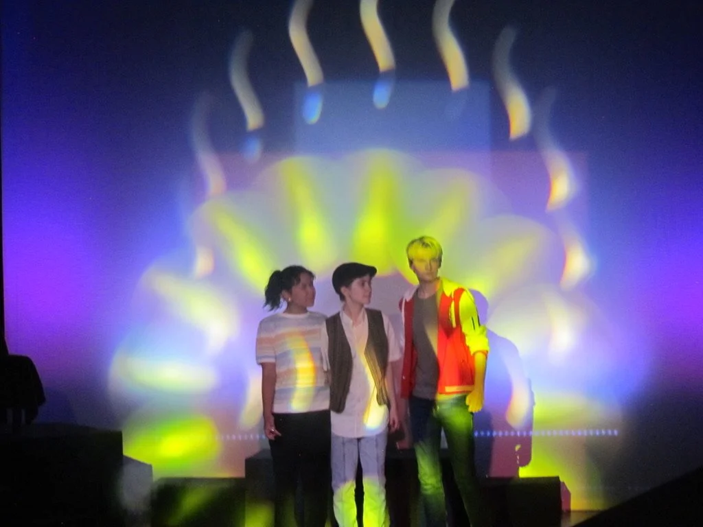 Three people with projections of colorful light and patterns on the wall behind them.