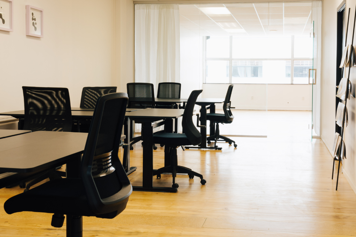 Modern office space with black chairs and tables, wooden floor, and natural light from large windows.