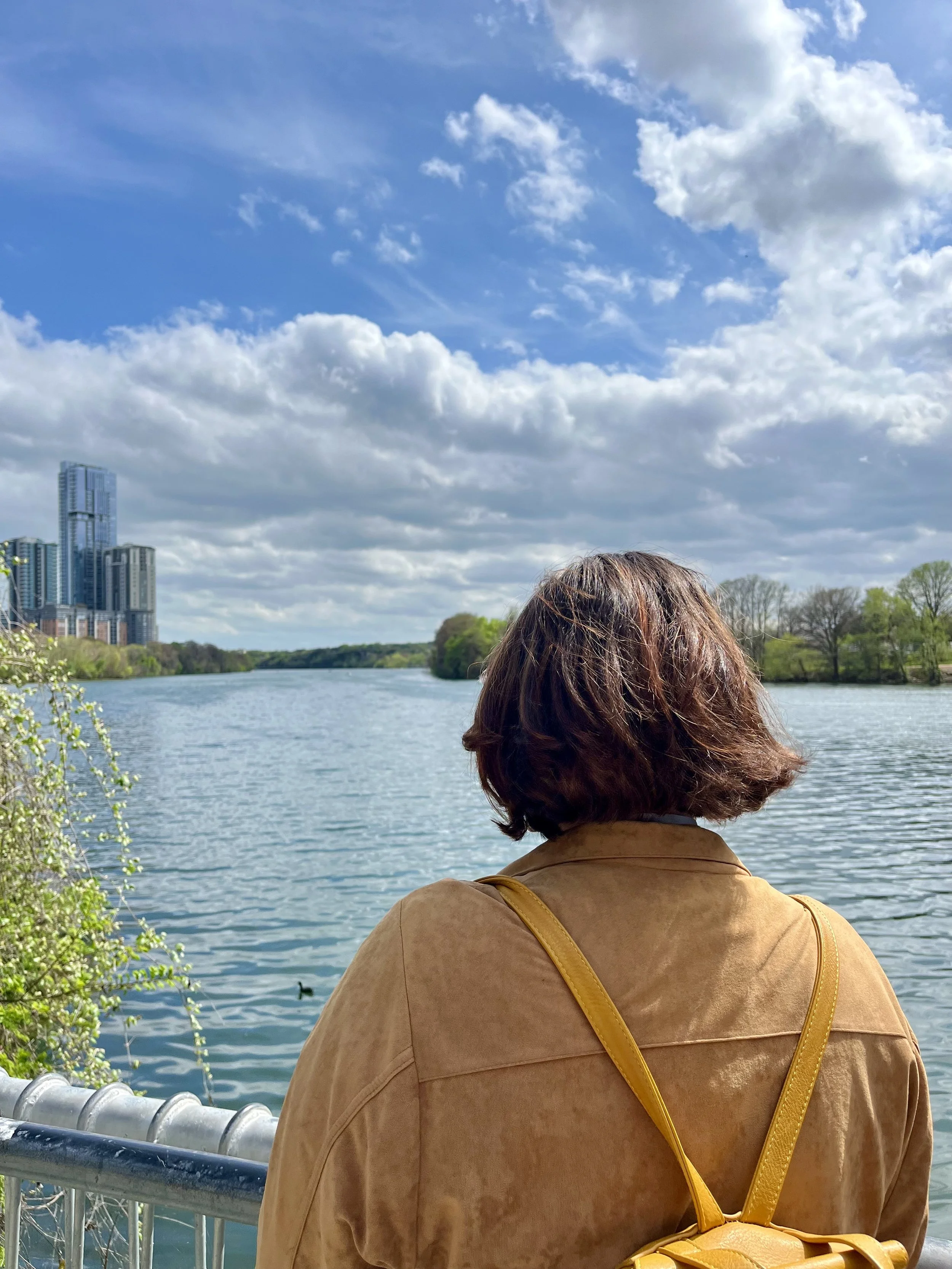 A woman with brown hair in a short bob haircut with a yellow backpack standing with her back to the camera as Lady Bird Lake in Austin unfolds ahead