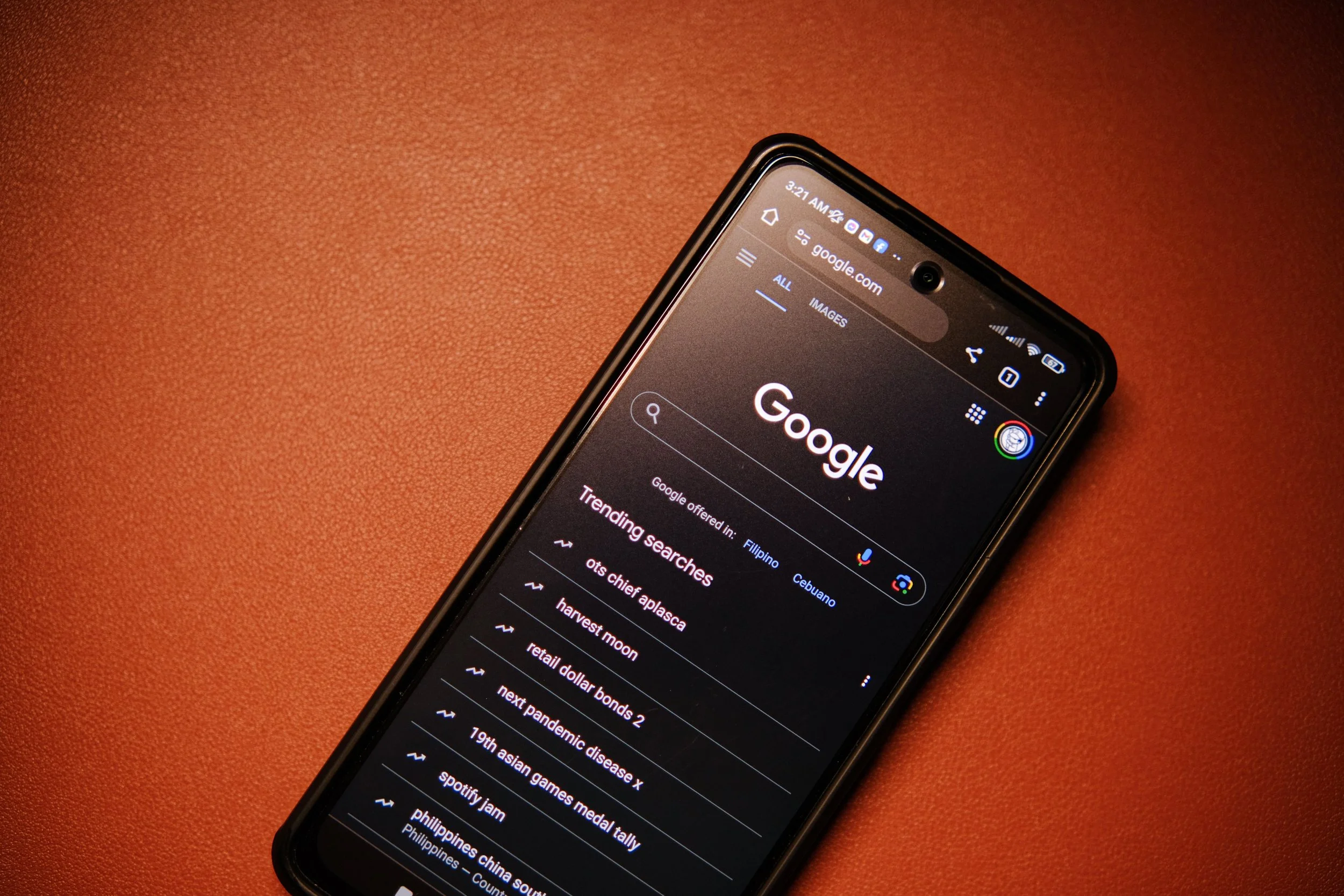 Close-up of a smartphone displaying a Google search page, placed on a reddish-brown surface.