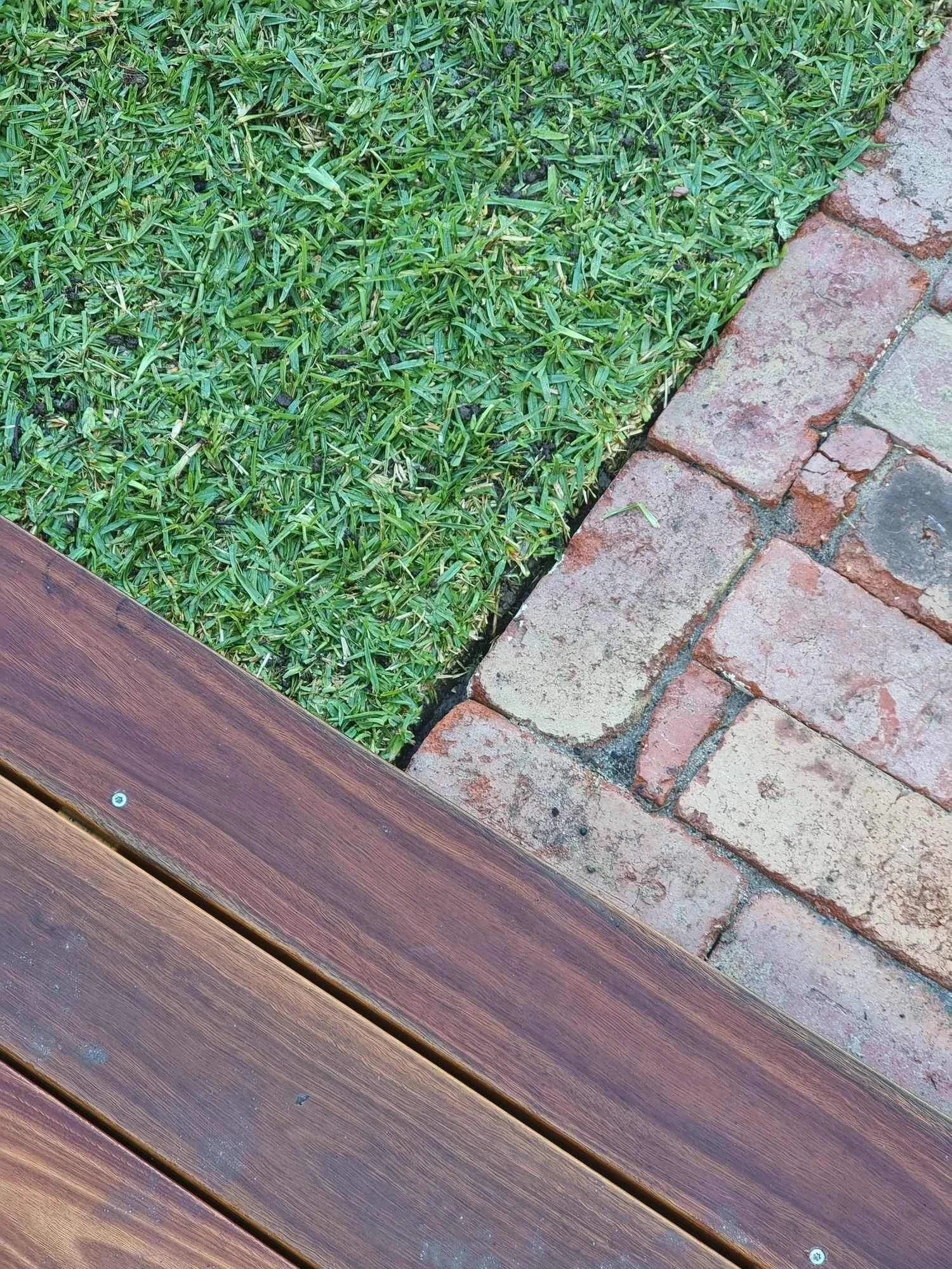 Close-up of wooden deck, red brick path, and green grass junction