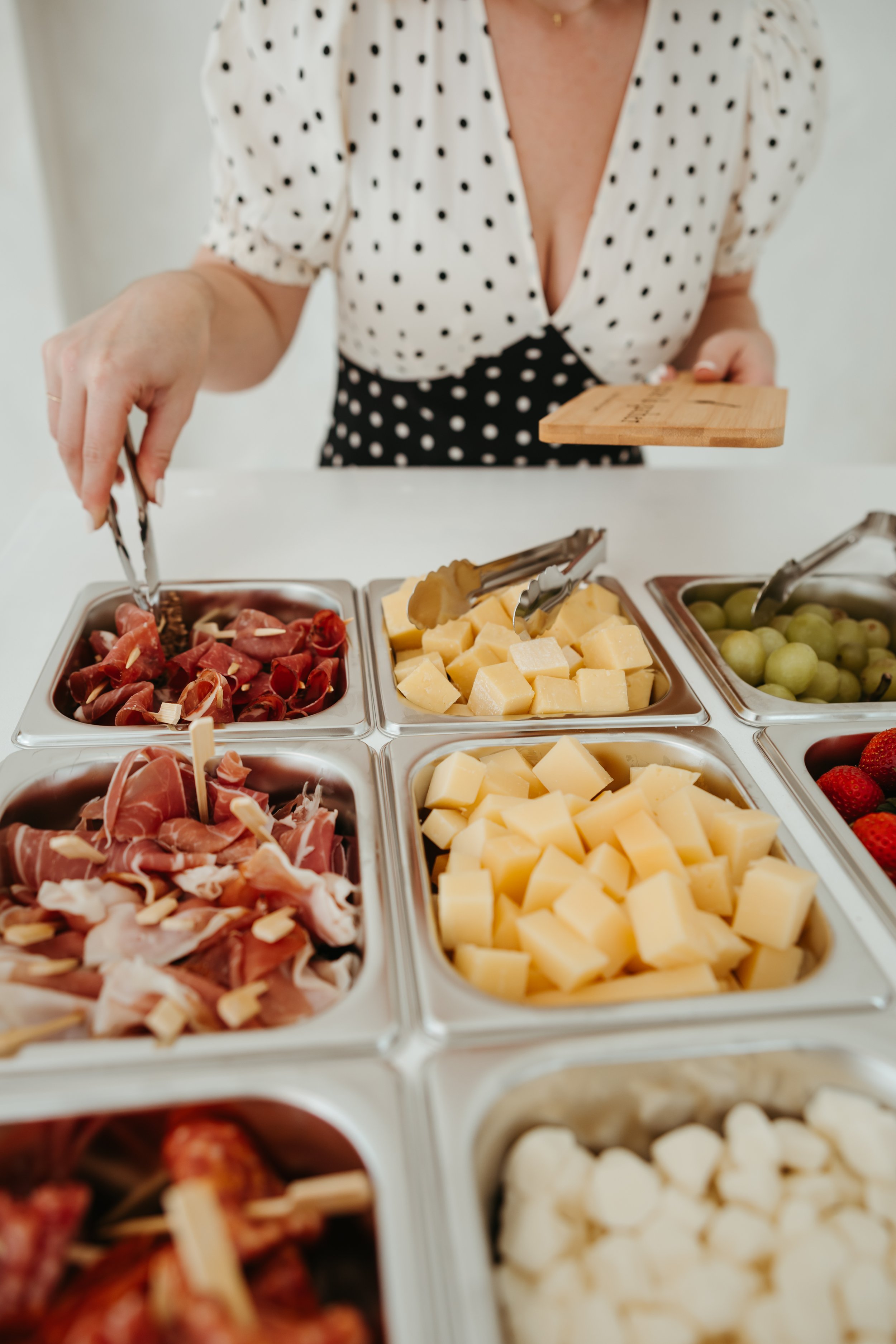 Person selecting food from a charcuterie spread, including cured meats, cheese cubes, grapes, and strawberries. - graze & gather | Luxury Charcuterie in Jacksonville, Florida