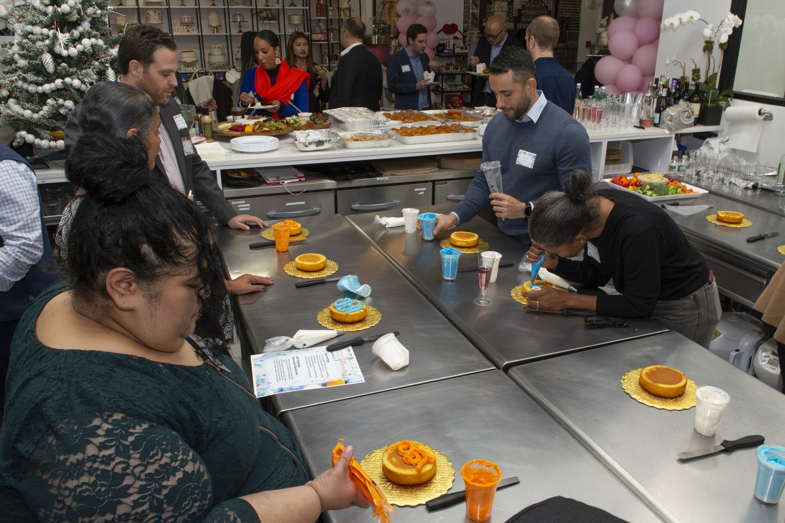 People decorating birthday cakes in a room decorated with balloons and a Christmas tree.