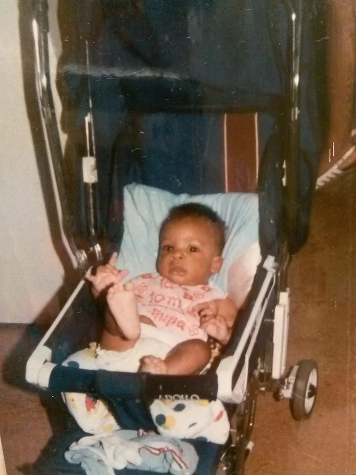 Baby Kareem Youngblood sitting in a stroller inside a Brooklyn home in the mid-1990s, early childhood moment tied to music, memory, and upbringing.